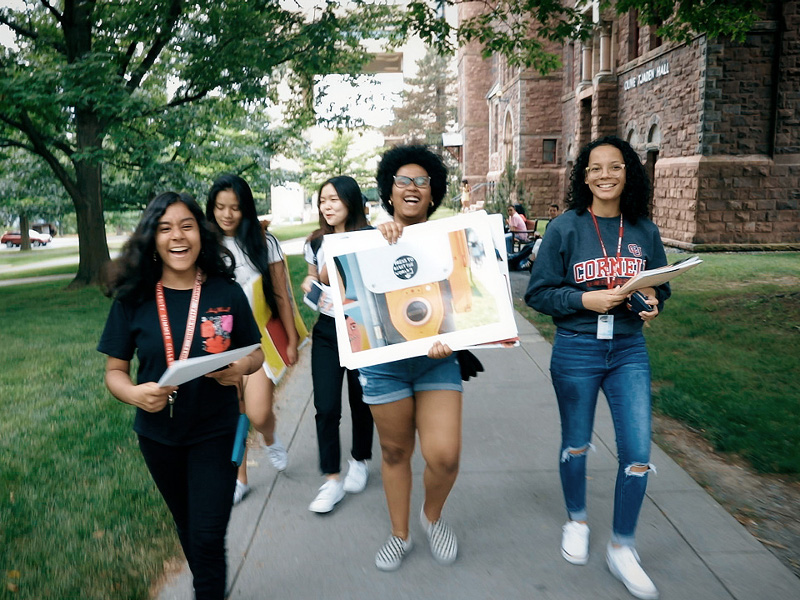 Five smiling students walking down the sidewalk at Cornell